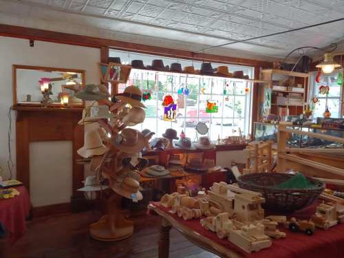 A cozy shop interior filled with wooden toys, hats on display, and colorful stained glass in the windows.