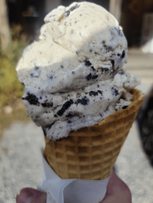 A close-up of a waffle cone filled with cookies and cream ice cream, featuring chunks of cookies.
