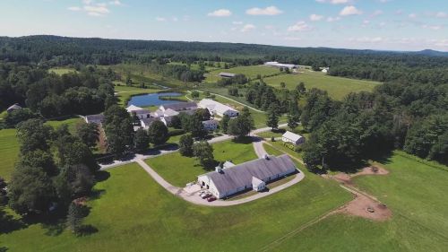Aerial view of a rural landscape featuring a farm with buildings, fields, and a pond surrounded by trees.
