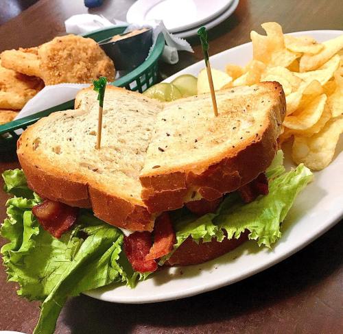 A sandwich with lettuce and bacon, served with potato chips and pickles on a plate.
