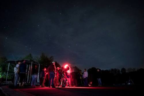 A group of people gathered at night, observing stars with telescopes under a dark sky filled with stars.