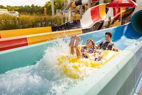 Two people enjoy a water slide, splashing through the water on a yellow inflatable tube at a water park.