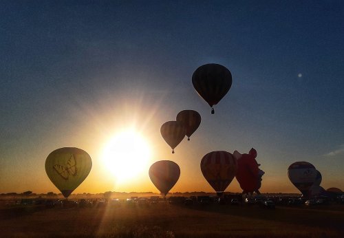 Hot air balloons silhouetted against a sunset, with a clear sky and grassy field below.