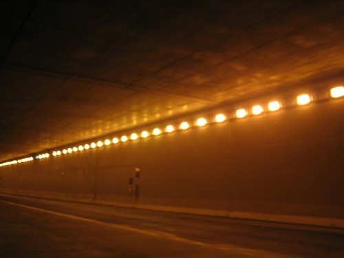 A dimly lit tunnel with a smooth ceiling and evenly spaced lights along the walls.