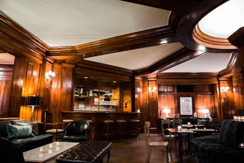 Elegant lounge with wooden paneling, plush seating, and a bar area, softly lit for a cozy atmosphere.