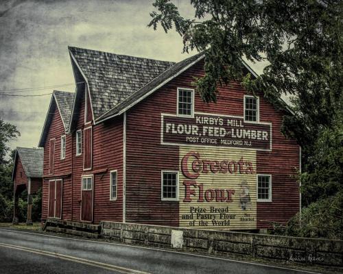 Red barn with vintage signage for "Kirby's Mill" and "Cresco Flour," set against a cloudy sky.