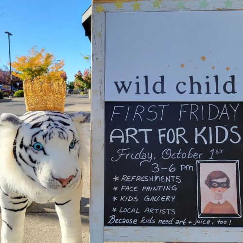 A white tiger statue wearing a crown next to a sign for a kids' art event on the first Friday of the month.