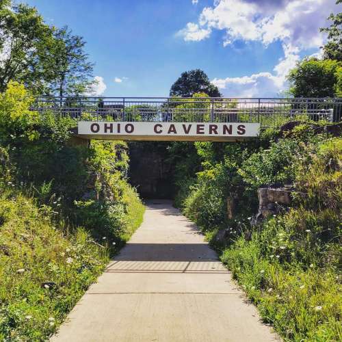 Entrance to Ohio Caverns, framed by lush greenery and a bright blue sky. Pathway leads into the cavern.