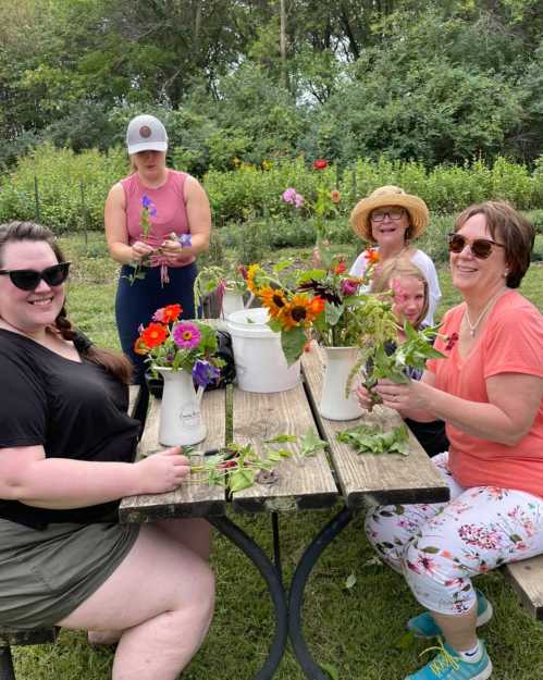 A group of women enjoying a flower arranging activity outdoors, surrounded by greenery and colorful blooms.