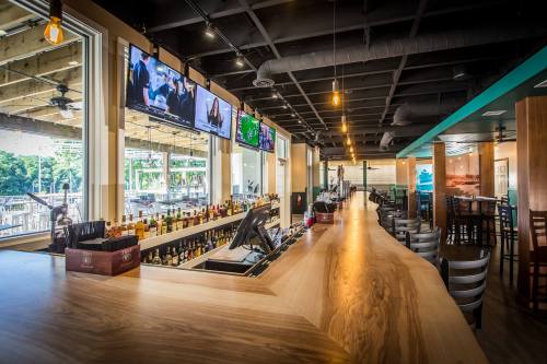A modern bar interior with a wooden counter, multiple TVs, and seating, featuring a bright and inviting atmosphere.