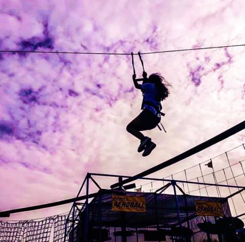 A person swings on a rope against a vibrant sky with clouds, enjoying an outdoor adventure activity.