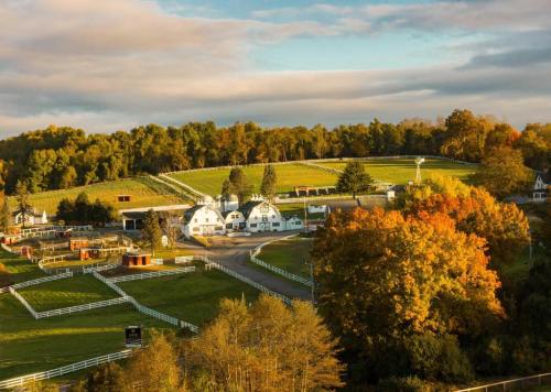 A scenic view of a farm with white fences, rolling hills, and colorful autumn trees under a cloudy sky.