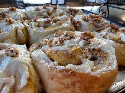 Close-up of freshly baked cinnamon rolls topped with cream cheese frosting and walnuts.