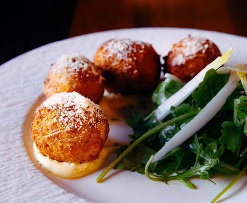 Four golden-brown fritters on a plate, served with a side of fresh greens and drizzled with sauce.