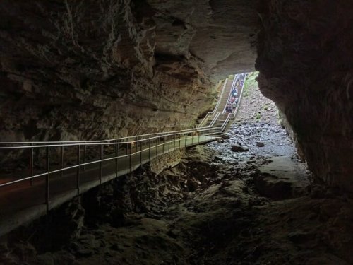 A dimly lit cave with a pathway leading out to bright light, surrounded by rocky walls and a gravel floor.