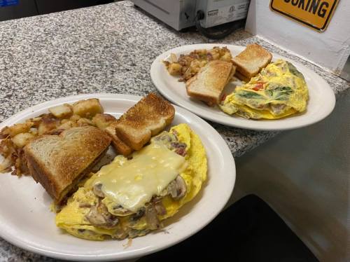 Two plates of breakfast: one with a cheesy mushroom omelet, toast, and hash browns; the other with a veggie omelet and toast.