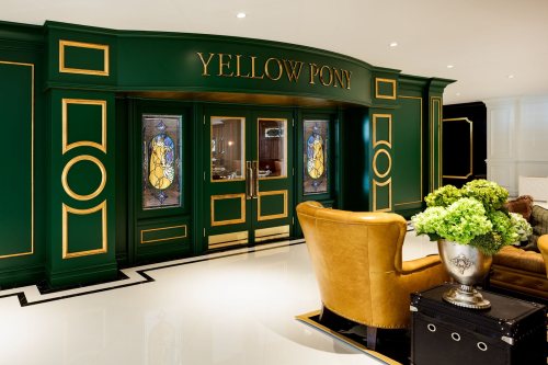 Elegant entrance of "Yellow Pony" featuring green walls, gold accents, and stained glass windows, with a cozy seating area.