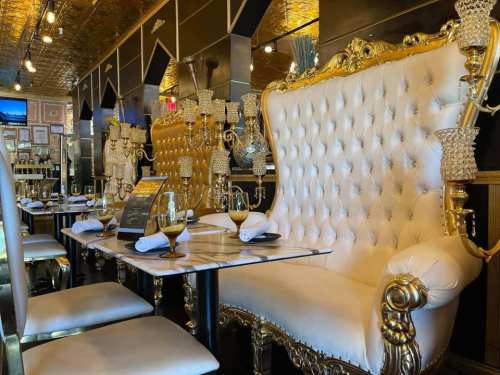 Luxurious restaurant interior featuring ornate golden decor, plush white seating, and elegant table settings.