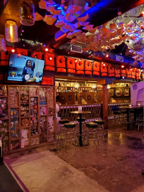 A cozy bar interior with colorful lights, a TV screen, and decorated walls featuring photos and hanging leaves.