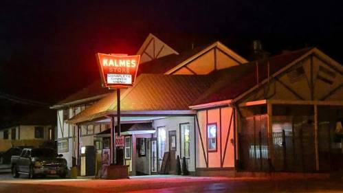 A brightly lit store at night with a red sign reading "Kalmes Store" and a visible menu.