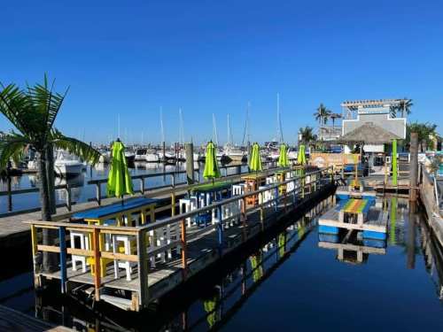 Colorful outdoor seating area by a marina, with boats in the background and bright umbrellas on a sunny day.