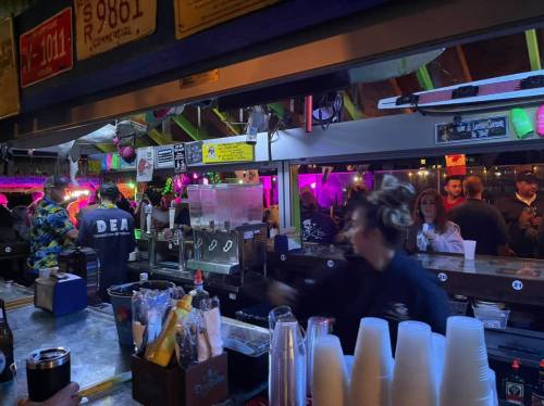 A lively bar scene with a bartender serving drinks, colorful lights, and patrons enjoying the atmosphere.