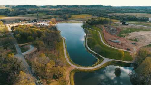 Aerial view of a winding river surrounded by greenery and fields, with a construction site in the background.