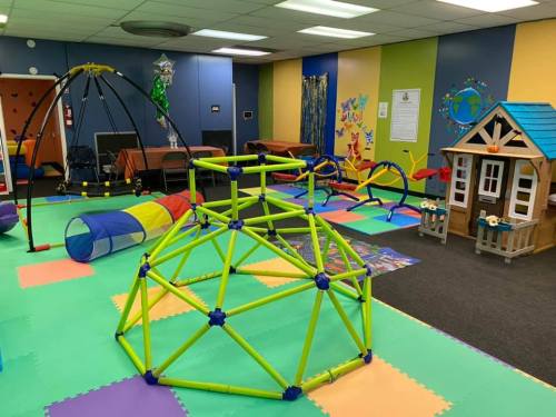 Colorful indoor play area with climbing structures, tunnels, and a playhouse on soft flooring.