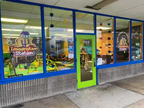 Bright storefront of "Imagination Station" with colorful decorations and play equipment visible through large windows.