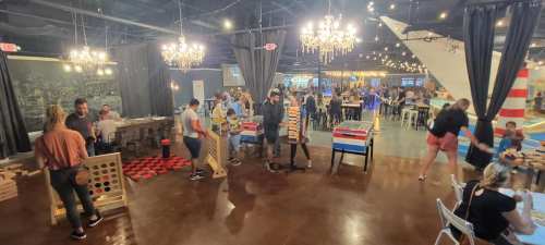 A lively indoor space with people playing games, dining, and enjoying a vibrant atmosphere with chandeliers and decor.