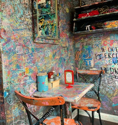 A colorful, graffiti-covered café corner with a small table, chairs, and a decorative mirror on the wall.