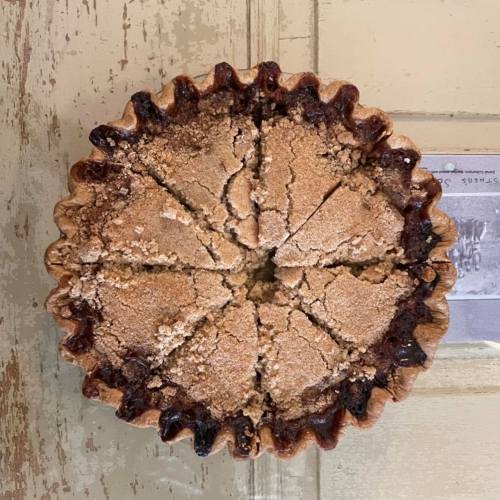 A round pie with a golden crust, sliced into wedges, showing a crumbly topping and a rustic wooden background.