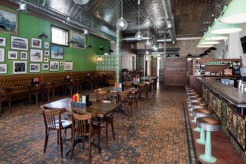 Interior of a restaurant featuring wooden tables, green walls, and vintage decor, with a bar area in the background.