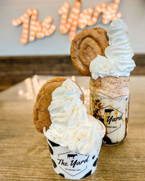 Two decadent milkshakes topped with whipped cream and cookies, set against a backdrop with "The Yard" sign.