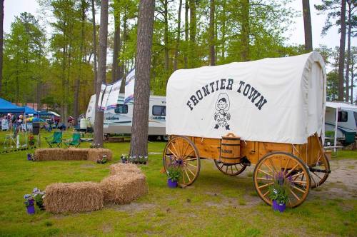 A wooden wagon labeled "Frontier Town" surrounded by hay bales and camping setups in a wooded area.