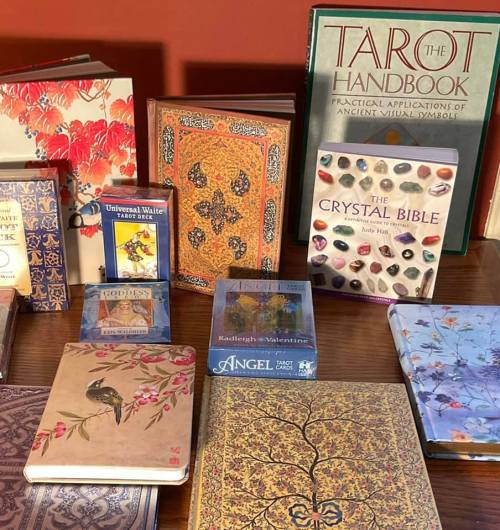 A collection of books on tarot, crystals, and spirituality, displayed on a wooden surface.