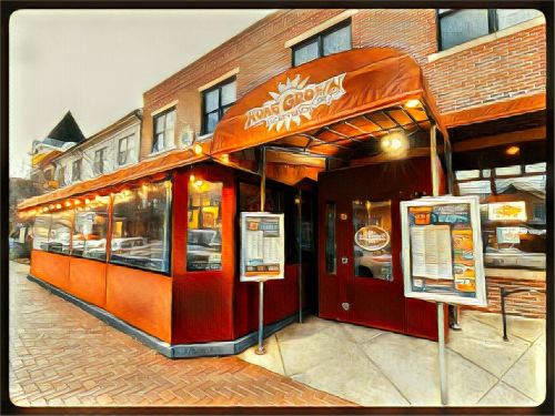 Exterior of a restaurant with an orange awning, large windows, and menu boards outside, set in a brick building.