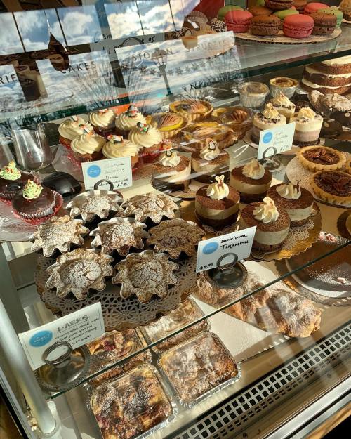 A display case filled with various desserts, including cupcakes, macarons, and layered cakes, all beautifully arranged.