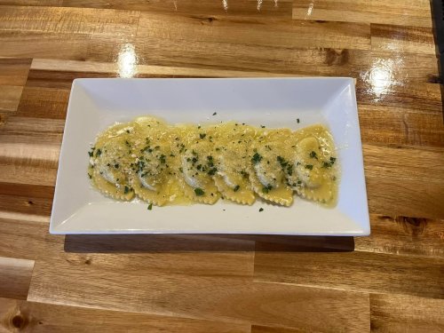 A plate of ravioli topped with a light sauce and sprinkled with herbs, served on a wooden table.