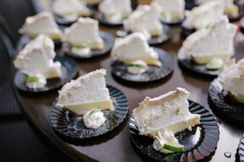 Slices of key lime pie on black plates, garnished with whipped cream and lime wedges, arranged on a table.