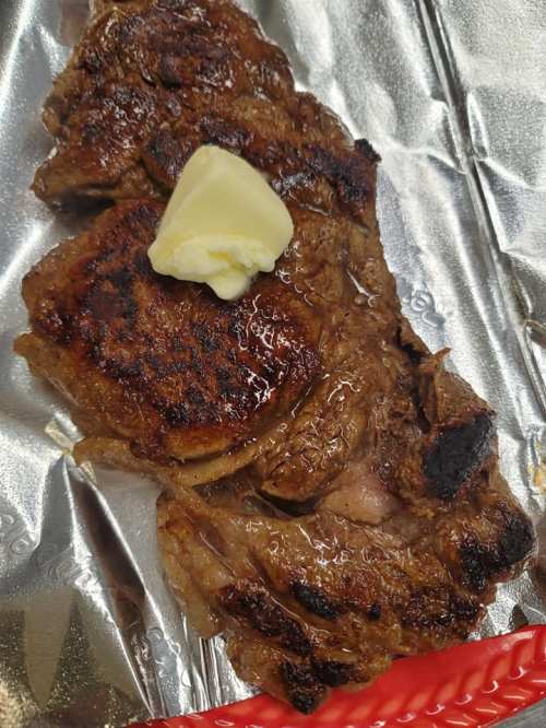 Grilled steak on foil, topped with a pat of butter, showcasing a rich, caramelized crust.