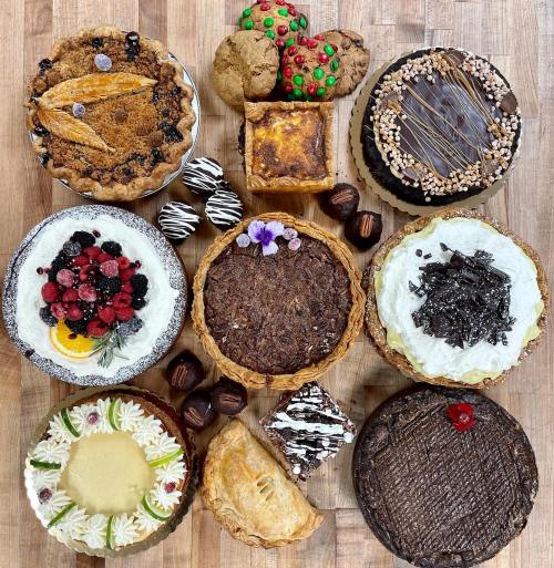 A variety of desserts including pies, cakes, cookies, and chocolates arranged on a wooden surface.