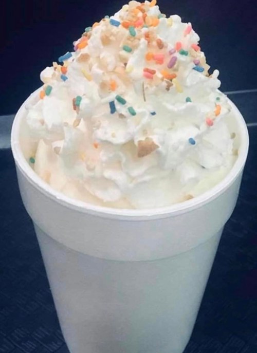 A white cup filled with creamy dessert topped with whipped cream and colorful sprinkles.