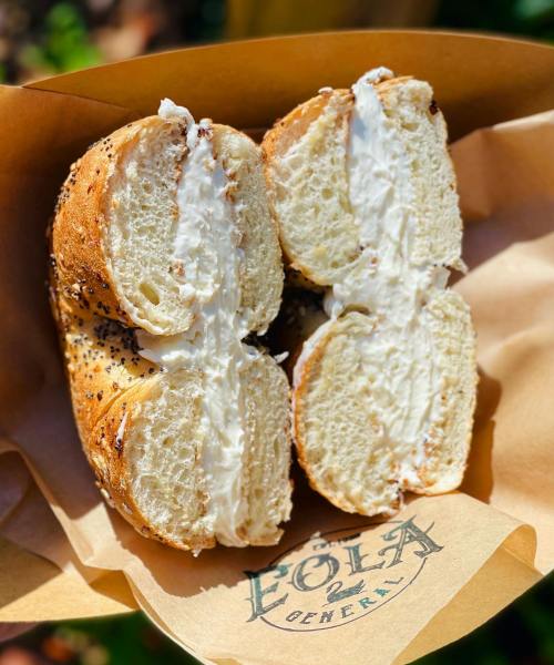 A freshly cut bagel with cream cheese, served in a paper wrapper with the logo of Eola General.