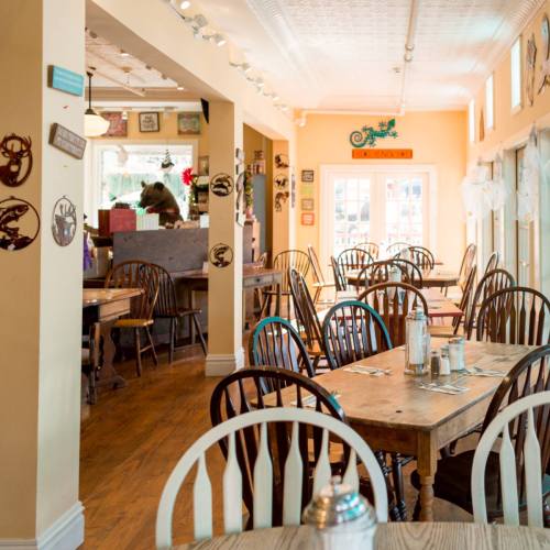 Cozy restaurant interior with wooden tables and chairs, warm lighting, and colorful decor on the walls.