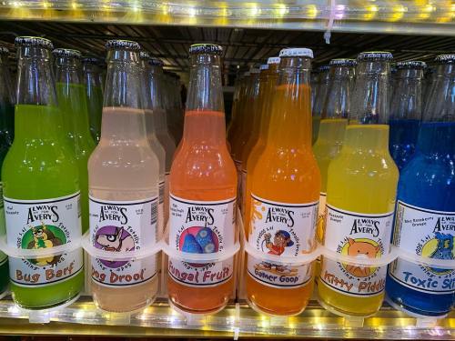 A shelf of colorful novelty soda bottles with playful labels like "Bug Bart," "Fungal Fruit," and "Toxic Slime."