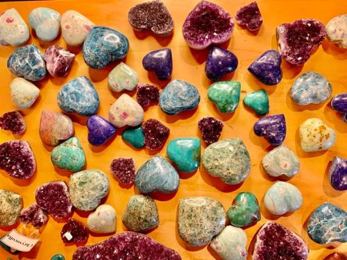 A colorful assortment of heart-shaped and irregularly shaped gemstones on a wooden surface.