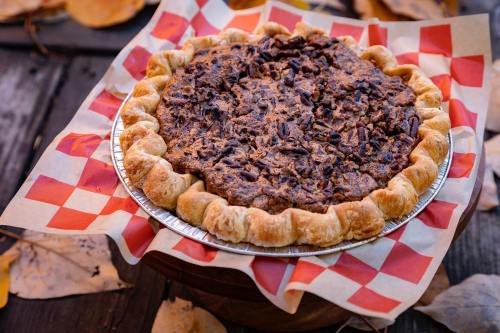 A freshly baked pecan pie on a checkered paper, surrounded by autumn leaves on a wooden surface.