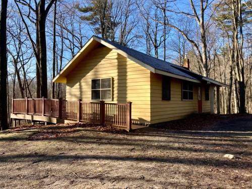 A yellow cabin surrounded by trees, featuring a wooden deck and a clear blue sky in the background.