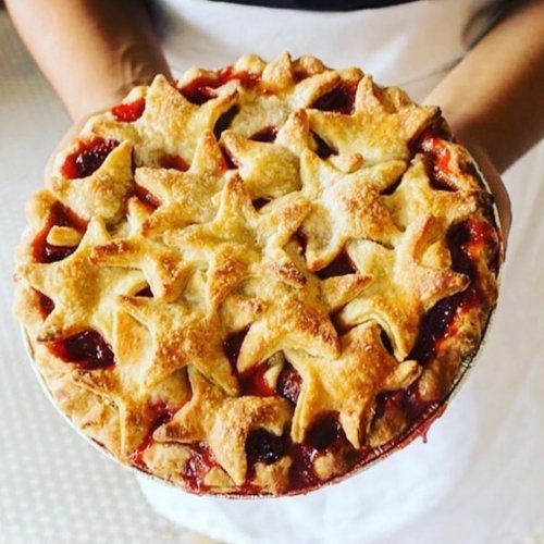 A freshly baked pie with a star-shaped crust, held by a person, showcasing a rich filling peeking through.